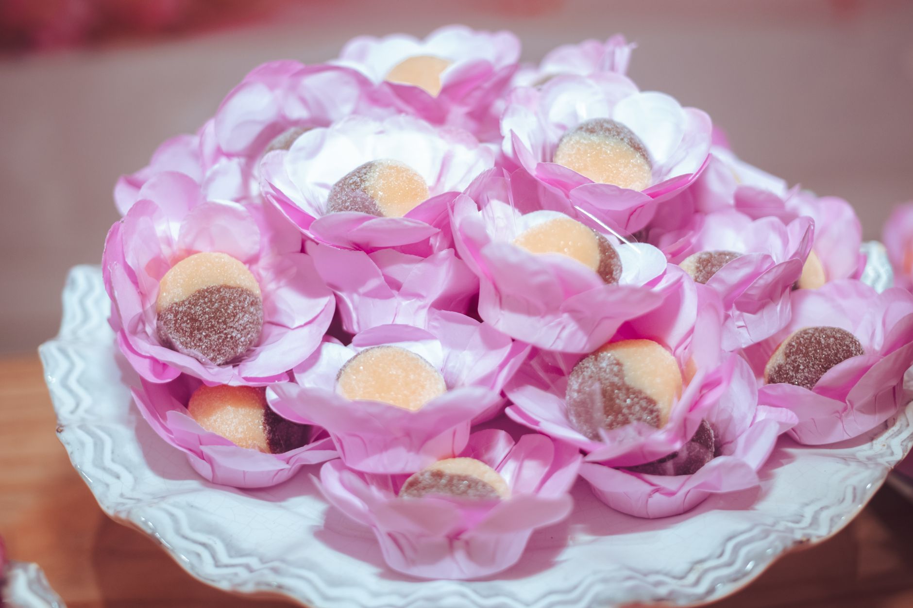 Elementos comemorativos tradicionais associados aos Erê na Umbanda: A close-up of assorted candies elegantly arranged in pink floral wrappers on a decorative plate.